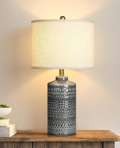 Gray ceramic table lamp with white linen shade and LED bulb on wooden surface